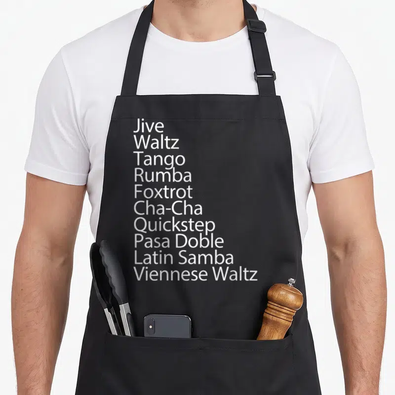 Ballroom traditional apron - White text listing Jive, Waltz, Tango, Rumba, Foxtrot, Cha-Cha, Quickstep, Pasa Doble — shown on a black cotton canvas apron against a white background