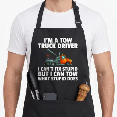 Tow driver operator truck apron - Cartoon orange tow truck surrounded by white text on grey background — shown on a black cotton canvas apron against a white background