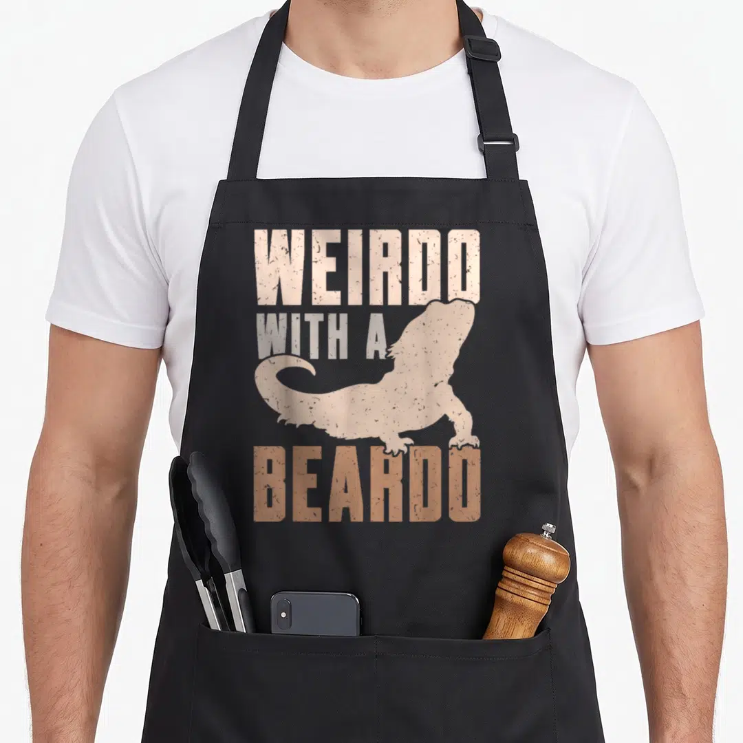 Weirdo dragon apron - Distressed text WEIRDO WITH A BEARDO around a beige bearded dragon silhouette on grey background — shown on a black cotton canvas apron against a white background