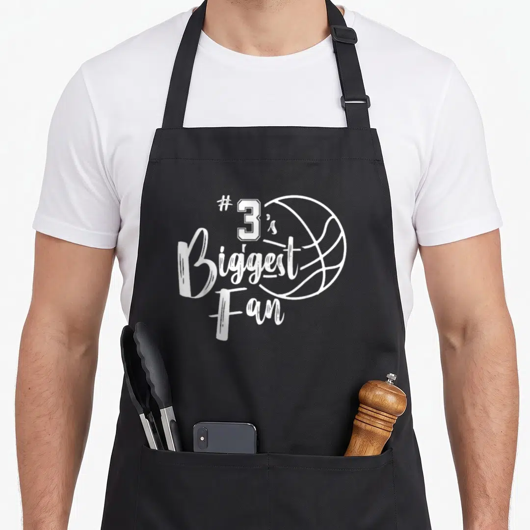 Three junior varsity apron - White #3's Biggest Fan text and basketball outline on black fabric — shown on a black cotton canvas apron against a white background
