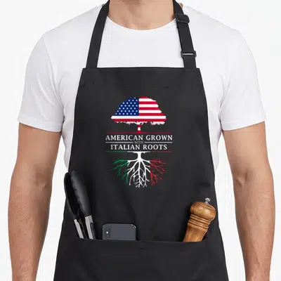 Root italy apron - Tree with US flag canopy and Italian colored roots separating text AMERICAN GROWN WITH ITALIAN ROOTS — shown on a black cotton canvas apron against a white background