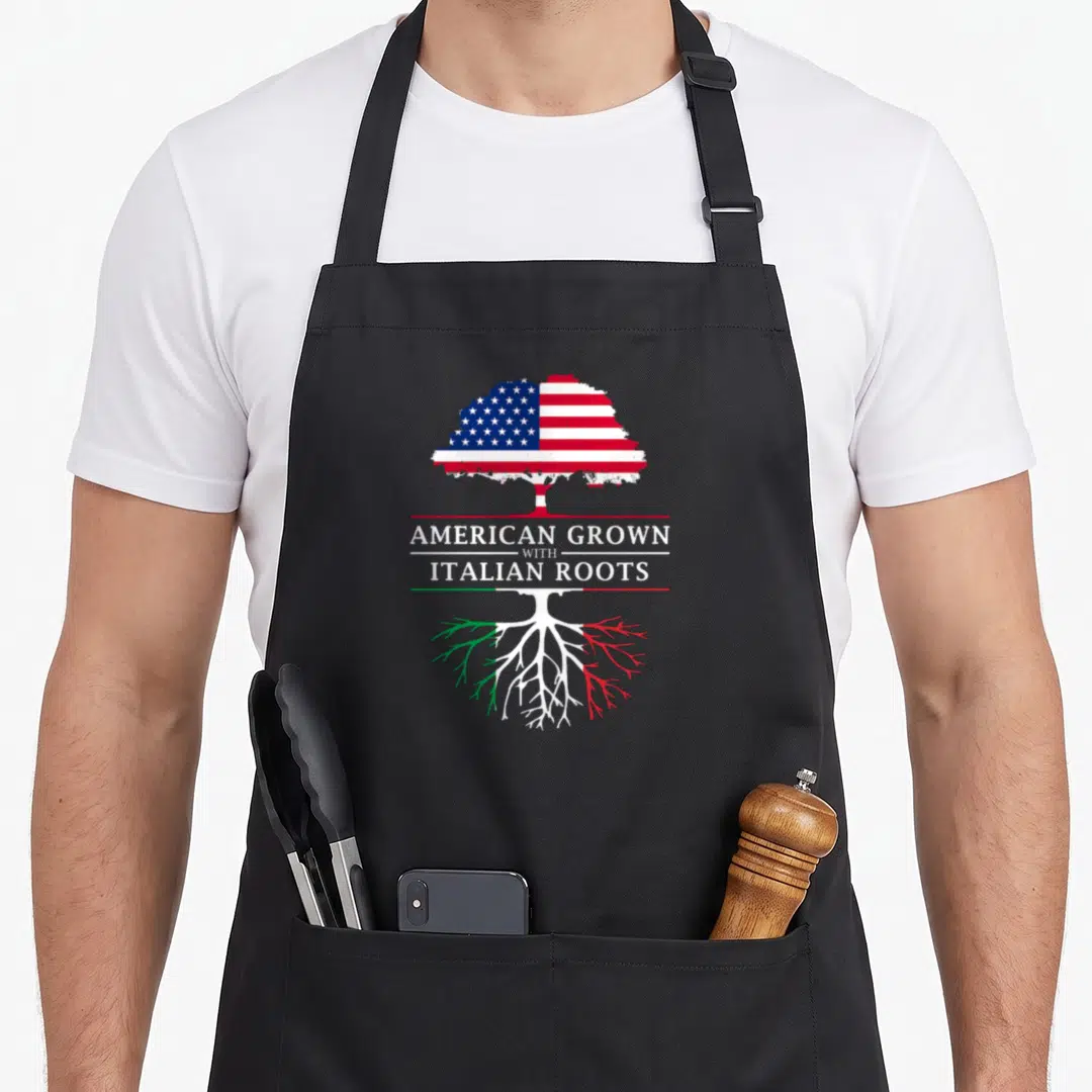 Root italy apron - Tree with US flag canopy and Italian colored roots separating text AMERICAN GROWN WITH ITALIAN ROOTS — shown on a black cotton canvas apron against a white background