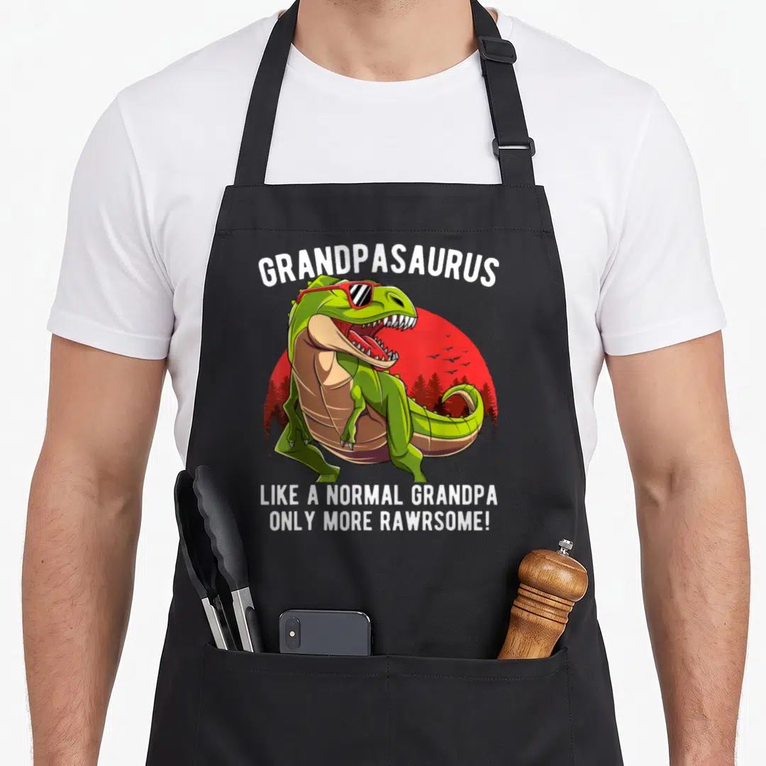 Normal grandpa apron - Green T-Rex with red sunglasses and Grandpasaurus pun text — shown on a black cotton canvas apron against a white background