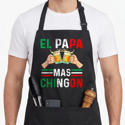 Chingon mexican apron - EL PAPA MAS CHINGON text with two clinking beer glasses and green white red stripes — shown on a black cotton canvas apron against a white background