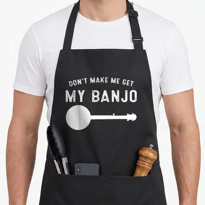 Music banjo apron - Distressed white text reading DON'T MAKE ME GET MY BANJO above banjo silhouette — shown on a black cotton canvas apron against a white background