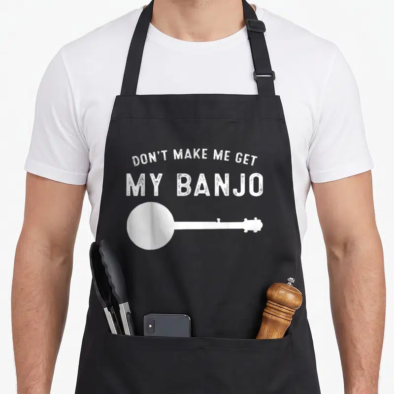 Music banjo apron - Distressed white text reading DON'T MAKE ME GET MY BANJO above banjo silhouette — shown on a black cotton canvas apron against a white background