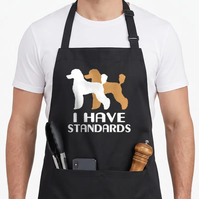 Toy poodle standard size of apron - Two overlapping poodle silhouettes in white and brown with stacked white text — shown on a black cotton canvas apron against a white background
