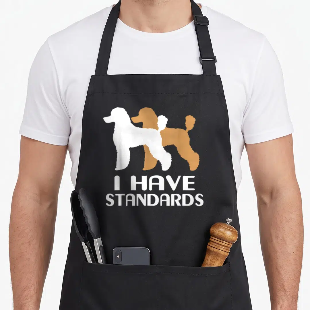 Toy poodle standard size of apron - Two overlapping poodle silhouettes in white and brown with stacked white text — shown on a black cotton canvas apron against a white background