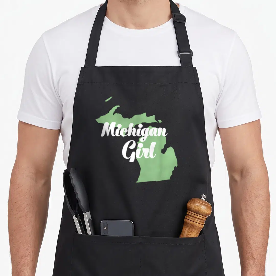 Michigan state pride apron - Light green Michigan map silhouette with white Michigan Girl script overlay — shown on a black cotton canvas apron against a white background