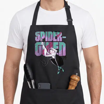 Spiderverse swing apron - Cartoon Spider-Gwen in white and black swinging in front of stacked purple and teal — shown on a black cotton canvas apron against a white background