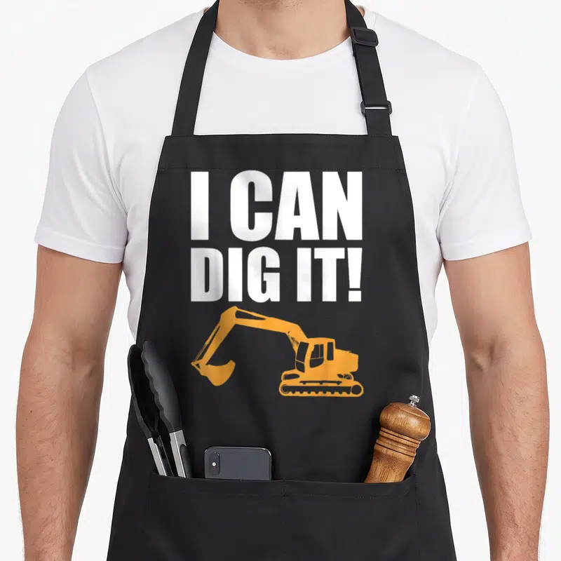 Landscaping construction apron - White I CAN DIG IT text above orange excavator silhouette — shown on a black cotton canvas apron against a white background
