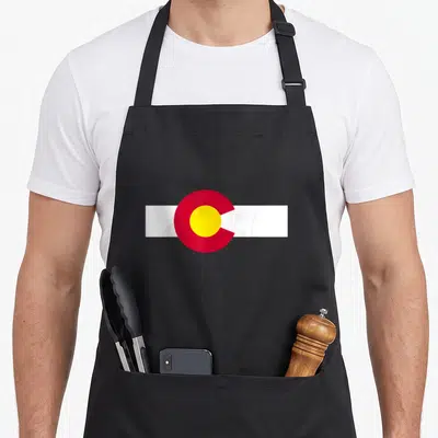Colorado state pride apron - Red circle with yellow center on white horizontal bar — shown on a black cotton canvas apron against a white background
