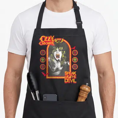 Osbourne devil's apron - Distressed red and yellow OZZY OSBOURNE SPEAK OF THE DEVIL text surrounding a central photo — shown on a black cotton canvas apron against a white background