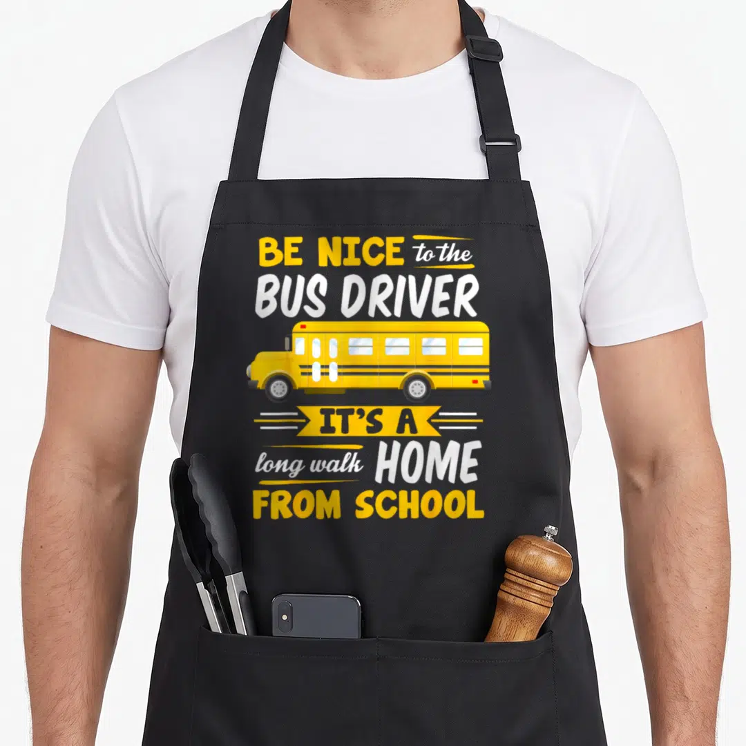 Driver school bus apron - Yellow cartoon school bus with text Be Nice to the Bus Driver It's A Long Walk Home — shown on a black cotton canvas apron against a white background
