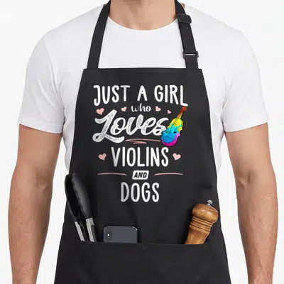 Violin dog apron - Stacked white text Just A Girl Who Loves Violins And Dogs with rainbow violin and pink hearts — shown on a black cotton canvas apron against a white background
