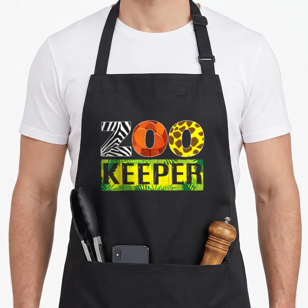 Safari halloween apron - ZOO KEEPER text with zebra stripe, orange swirl, giraffe spot, and jungle leaf patterns — shown on a black cotton canvas apron against a white background