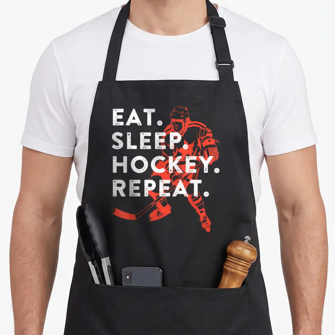 Eat frappe apron - Red hockey player silhouette behind four lines of white text reading EAT SLEEP HOCKEY REPEAT — shown on a black cotton canvas apron against a white background