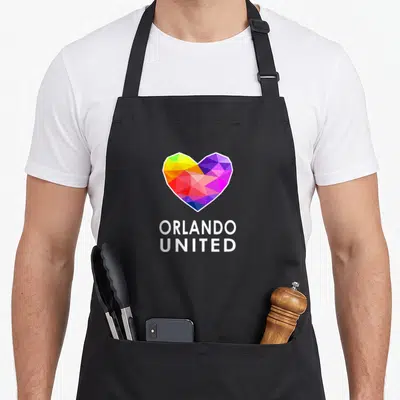Pulse pride apron - Geometric rainbow heart above stacked white text ORLANDO UNITED — shown on a black cotton canvas apron against a white background