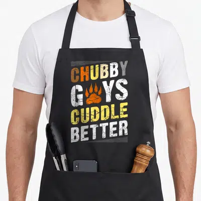Bear community gay pride apron - Distressed text Chubby Guys Cuddle Better with orange paw print replacing the U in Guys — shown on a black cotton canvas apron against a white background