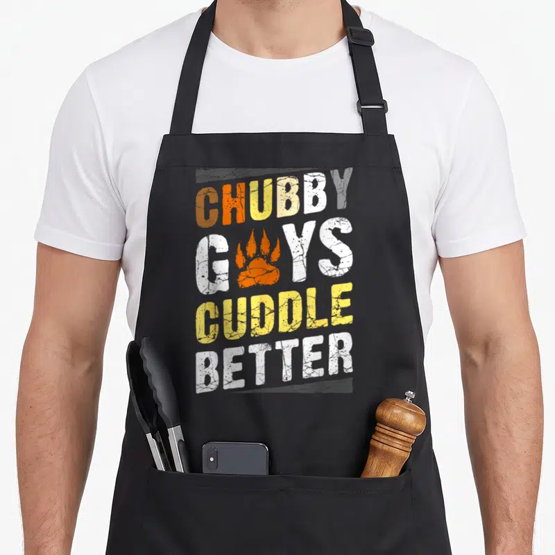 Bear community gay pride apron - Distressed text Chubby Guys Cuddle Better with orange paw print replacing the U in Guys — shown on a black cotton canvas apron against a white background