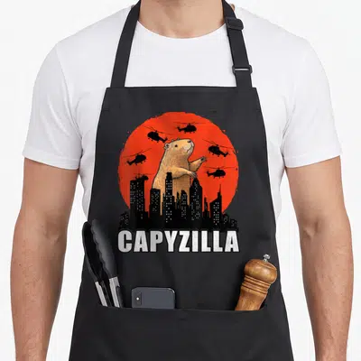 Rodent cute capybara apron - Giant brown capybara behind black skyline with red sun and five helicopters — shown on a black cotton canvas apron against a white background