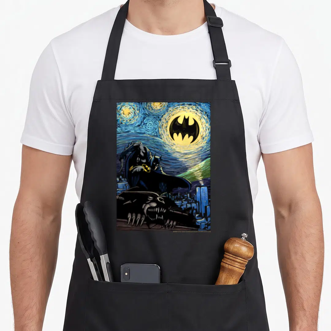 Painting nights apron - Watercolor Batman crouching on gargoyle under swirling blue yellow moon with city buildings — shown on a black cotton canvas apron against a white background