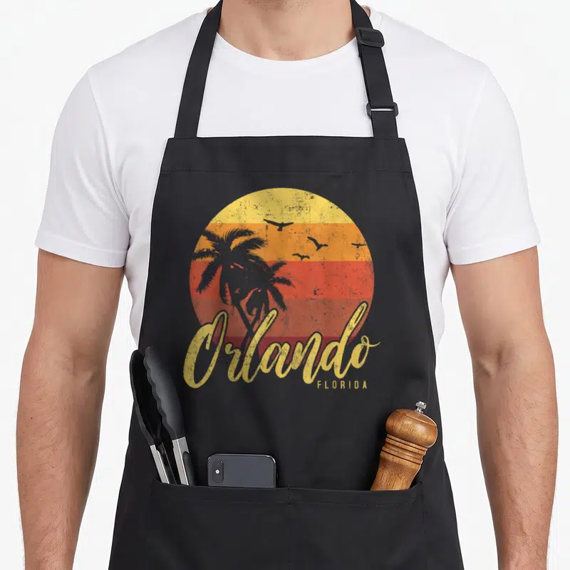 Cool orlando florida apron - Retro striped sun with grey palm tree and Orlando script text — shown on a black cotton canvas apron against a white background