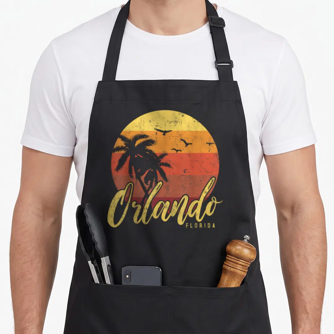 Cool orlando florida apron - Retro striped sun with grey palm tree and Orlando script text — shown on a black cotton canvas apron against a white background