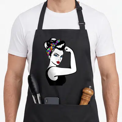 Autism rosie the riveter apron - Cartoon woman flexing arm wearing multi-colored puzzle pattern headband in bright — shown on a black cotton canvas apron against a white background