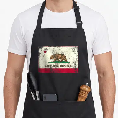 Cali california apron - Distressed California Republic flag print with brown bear, red star, and text on white field — shown on a black cotton canvas apron against a white background