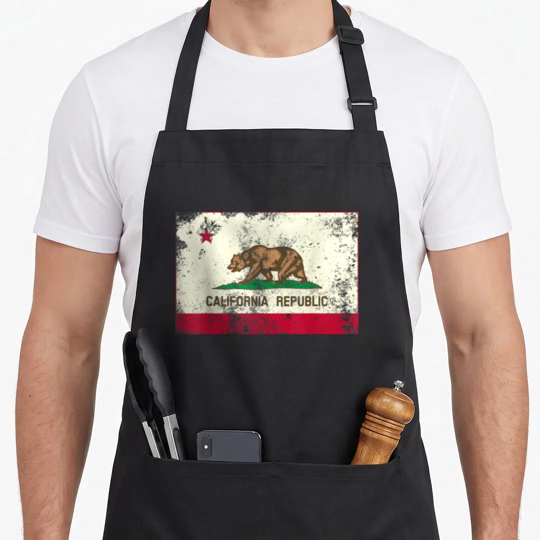Cali california apron - Distressed California Republic flag print with brown bear, red star, and text on white field — shown on a black cotton canvas apron against a white background
