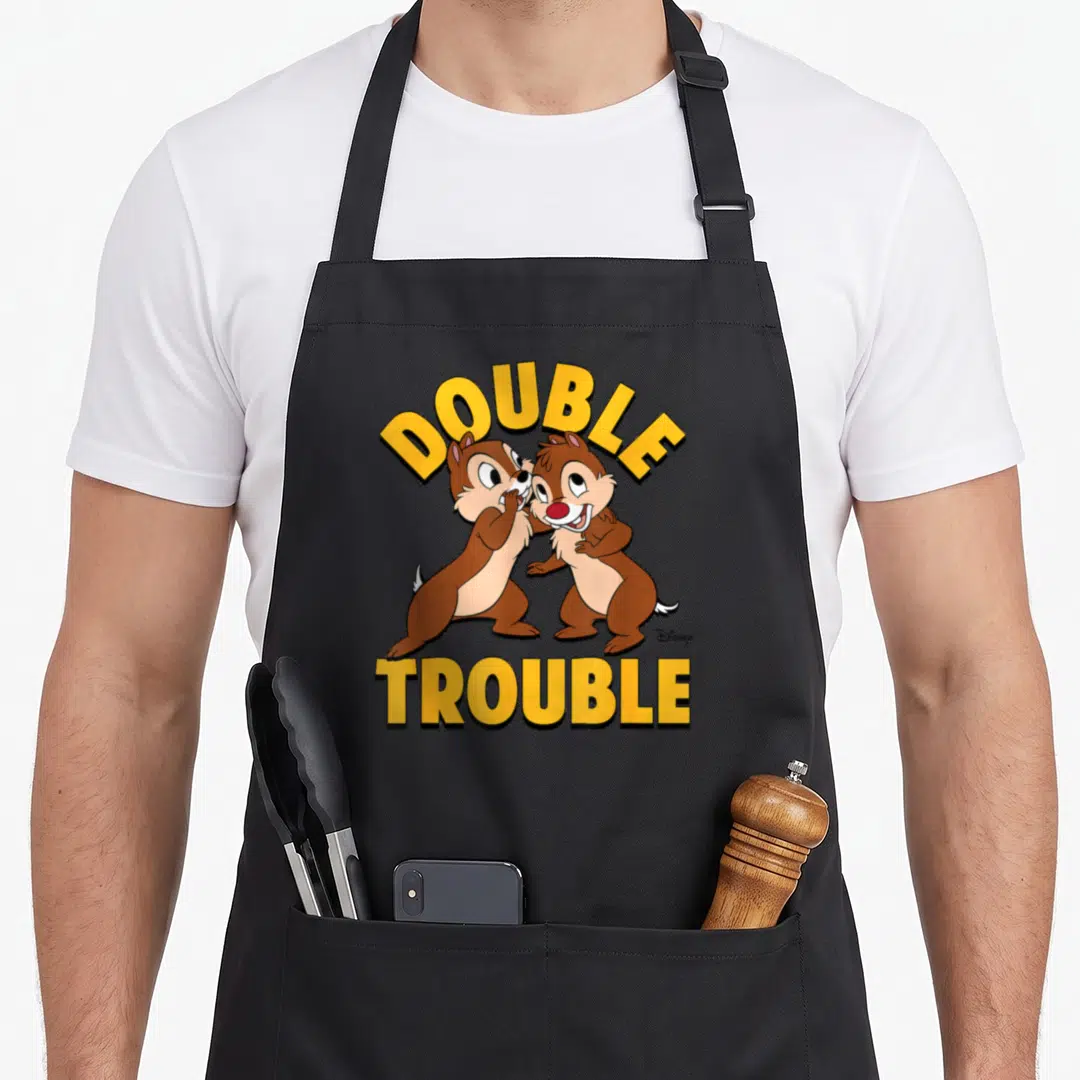 Chip double apron - Two brown chipmunks with yellow arched DOUBLE TROUBLE text in cartoon style — shown on a black cotton canvas apron against a white background