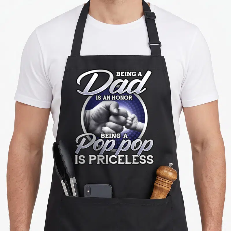 Priceless father day apron - Dad Pop Pop honor text surrounding a fist bump photo of adult and baby hands — shown on a black cotton canvas apron against a white background