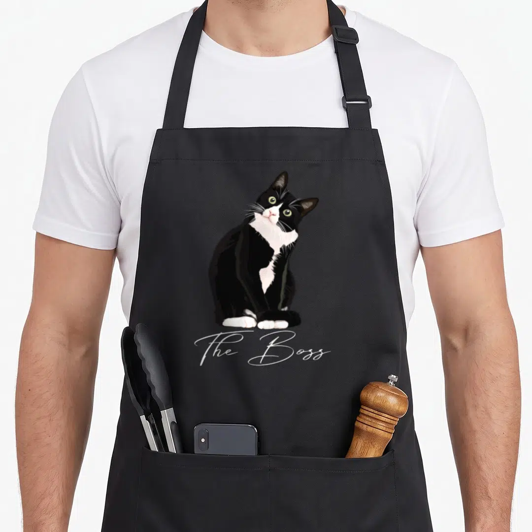Funny boss tuxedo apron - Realistic black and white cat sitting above white script text The Boss — shown on a black cotton canvas apron against a white background