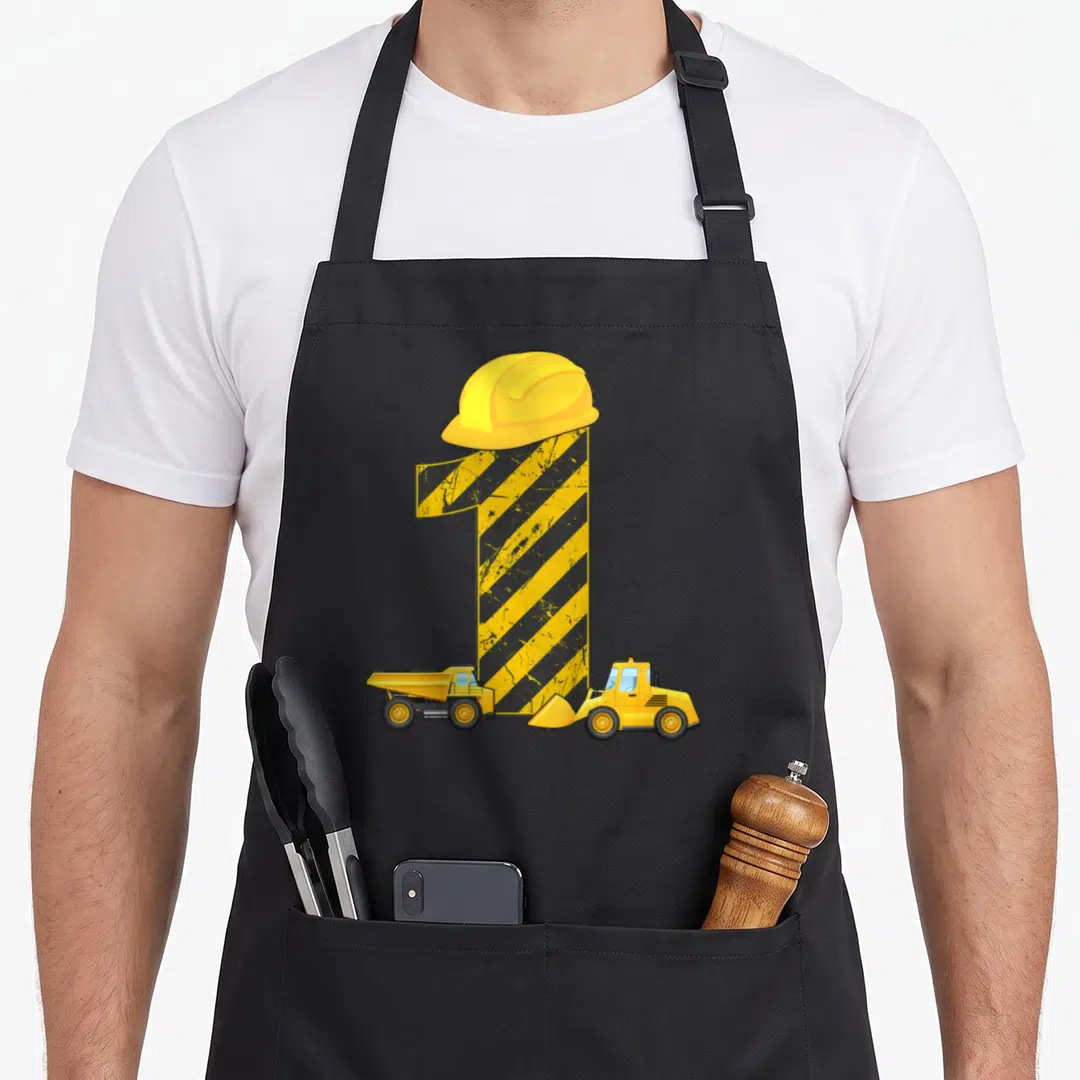 Builder birthday apron - Number 1 with hard hat, dump truck, and bulldozer in yellow black stripes — shown on a black cotton canvas apron against a white background