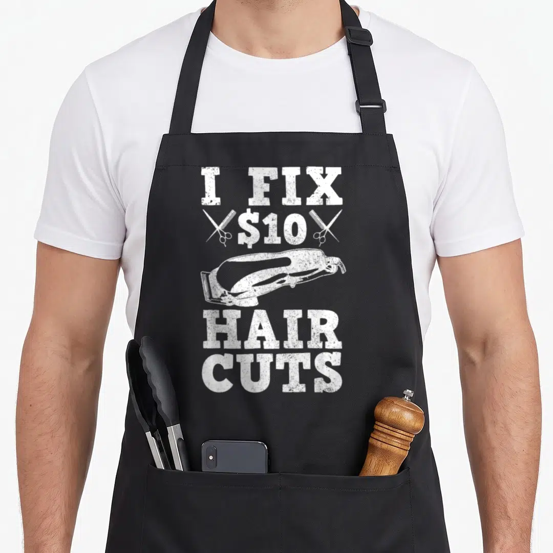 Hairdresser barber apron - White distressed I Fix $10 Hair Cuts text with central hair clipper and crossed scissors — shown on a black cotton canvas apron against a white background