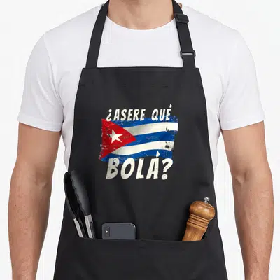 Flag spanish aprons - Distressed Cuba flag in blue white red with ¿ASERE QUÉ BOLA? text above and below — shown on a black cotton canvas apron against a white background