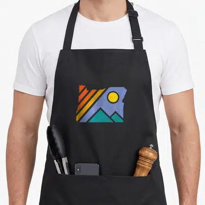 Throwback oregon dunes apron - Oregon state map silhouette with red orange yellow blue stripes and teal mountains — shown on a black cotton canvas apron against a white background