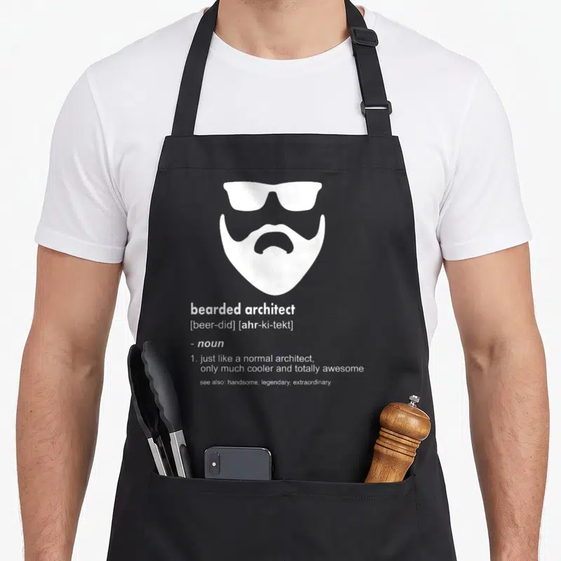 Architect beard apron - White bearded face with sunglasses and dictionary definition text — shown on a black cotton canvas apron against a white background