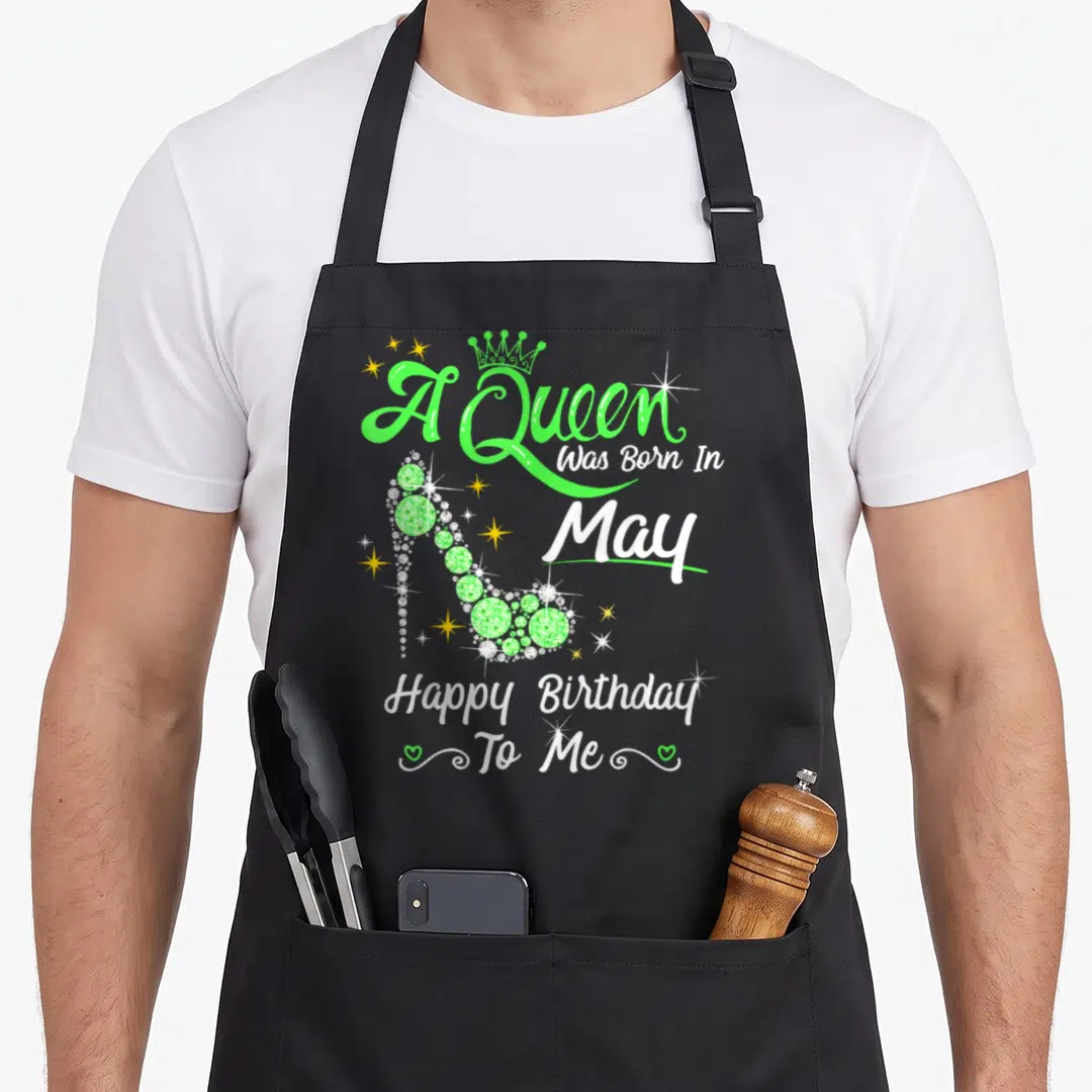 May birthday baking queen apron - Green high heel shoe with A Queen Was Born In May text and hearts — shown on a black cotton canvas apron against a white background