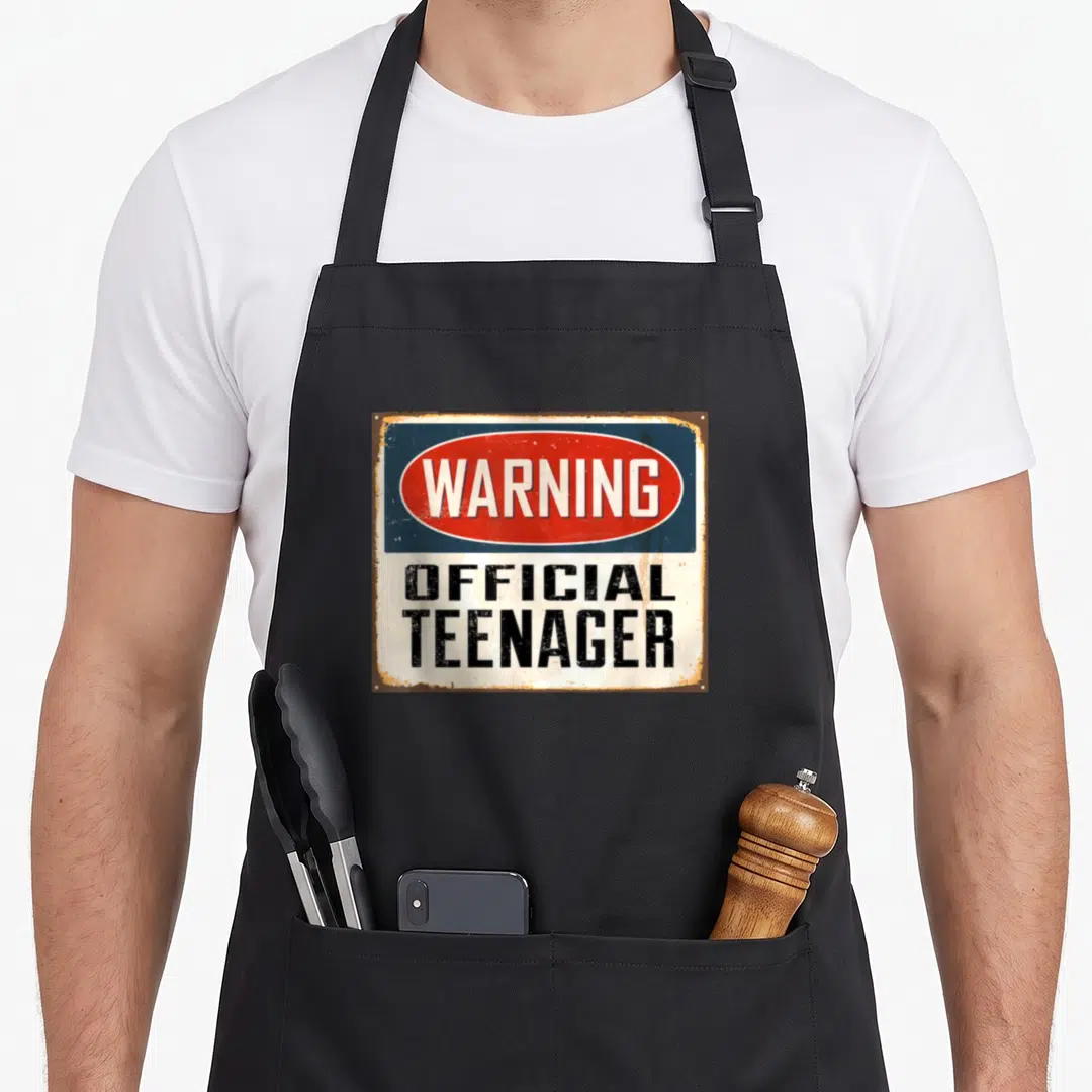 Warning birthday apron - Retro sign reading WARNING OFFICIAL TEENAGER in red white blue and black — shown on a black cotton canvas apron against a white background