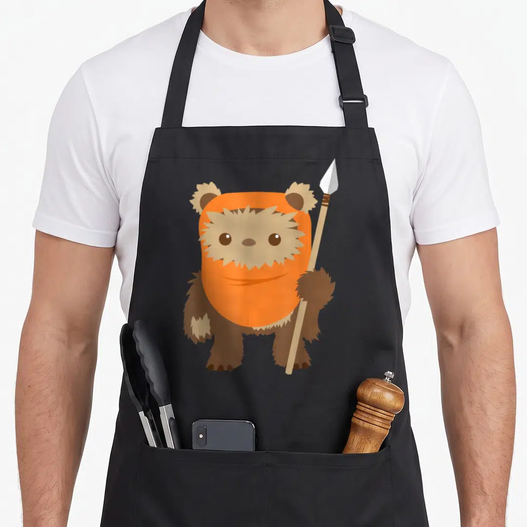 Wicket kawaii apron - Cartoon bear in orange hood holding a wooden spear — shown on a black cotton canvas apron against a white background