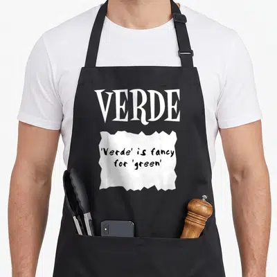 Verde halloween apron - White torn paper graphic with black text reading Verde is fancy for green under large white — shown on a black cotton canvas apron against a white background