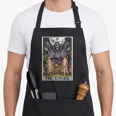 Grim halloween apron - The Lovers tarot card print with central Grim Reaper, purple robes, and figures by a fire — shown on a black cotton canvas apron against a white background