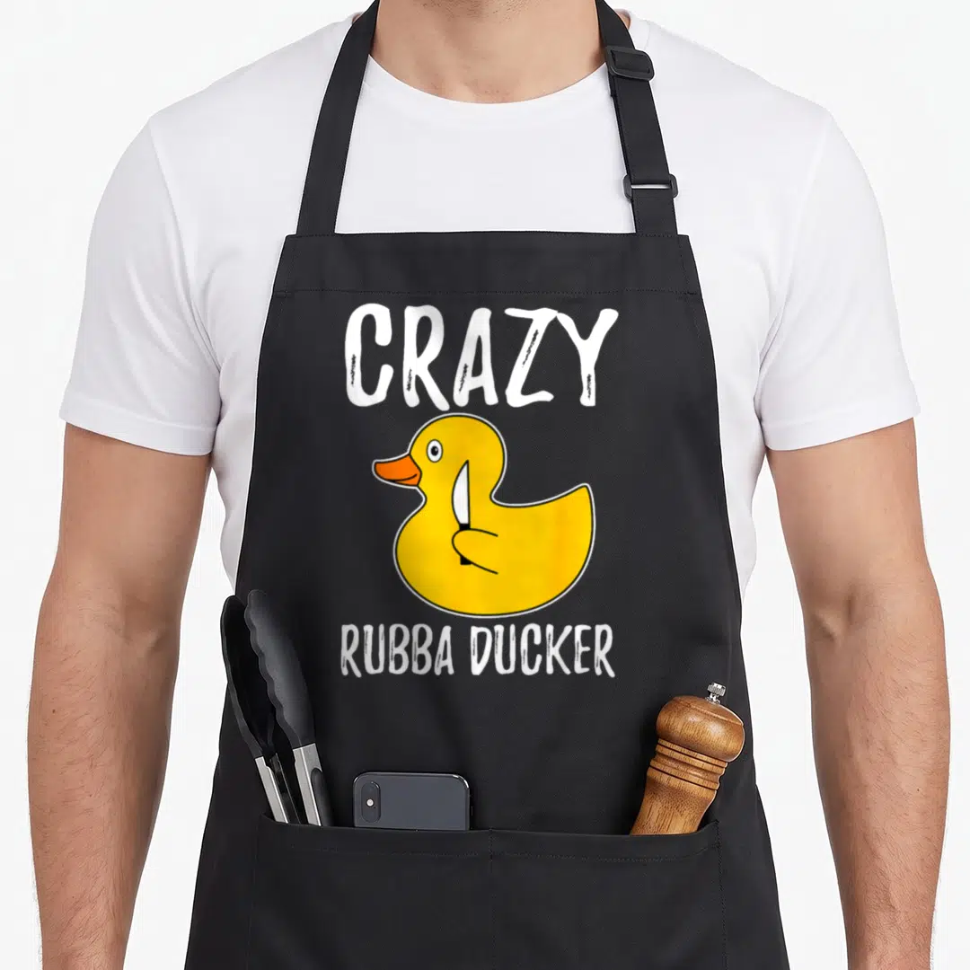 Rubba cotton duck aprons - Yellow rubber duck holding knife between CRAZY RUBBA DUCKER text lines — shown on a black cotton canvas apron against a white background