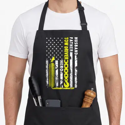 Hero american flag apron - Husband Father Tow Driver Hero text with yellow chain and light bar on distressed flag — shown on a black cotton canvas apron against a white background