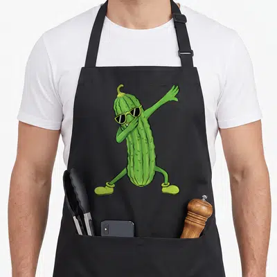 Dabbing pickle apron - Cartoon green pickle wearing sunglasses and shoes in a dab pose — shown on a black cotton canvas apron against a white background