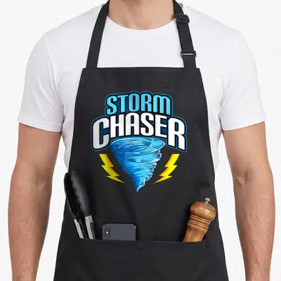 Storm hurricane apron - Blue tornado graphic with STORM CHASER text and yellow lightning bolts — shown on a black cotton canvas apron against a white background