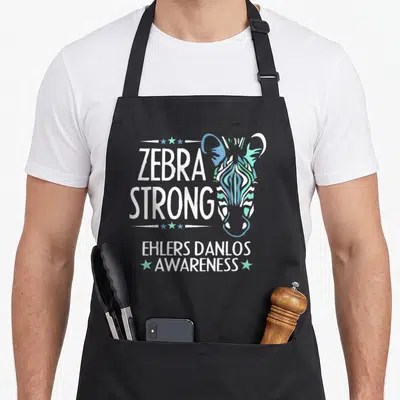 Danlo zebra apron - Stylized zebra head in teal blue green next to ZEBRA STRONG EHLERS DANLOS AWARENESS text with stars — shown on a black cotton canvas apron against a white background