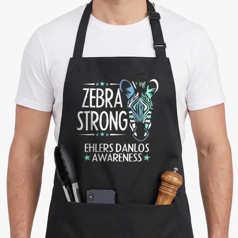 Danlo zebra apron - Stylized zebra head in teal blue green next to ZEBRA STRONG EHLERS DANLOS AWARENESS text with stars — shown on a black cotton canvas apron against a white background